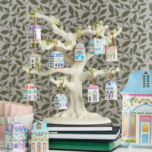 Decorative tree with small house ornaments against a leaf-patterned wall.